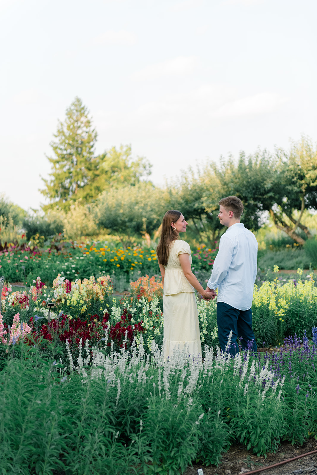 Couple holding hands during a summer engagement session at Stan Hywet Gardens in Akron, Ohio, surrounded by colorful garden flowers.